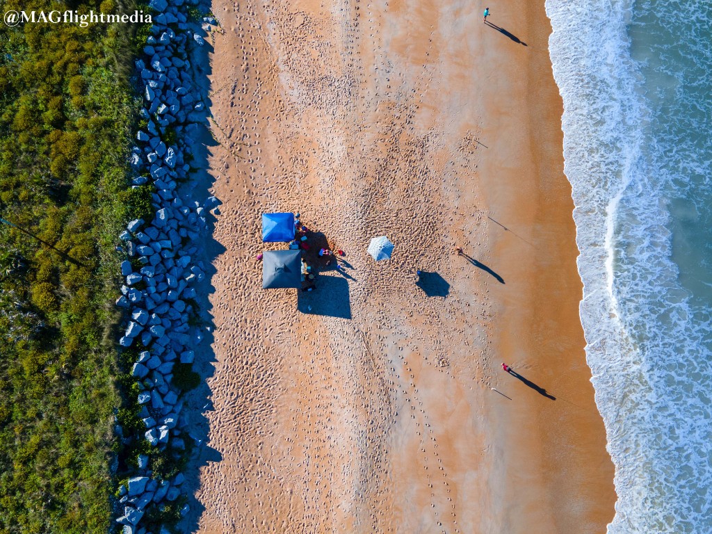 Aerial view of Flagler Beach, umbrellas set up on the sand next to the rock jetty